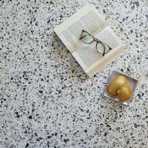 Terrazzo Eden Carodeco fond blanc avec éclats verts et beige utilisé en plan de travail avec livre et accessoires déco